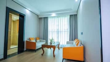 A modern living room with two sofas, one orange and one white, a wooden coffee table, and a large window with curtains.