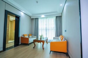 Una sala de estar moderna con dos sofás, uno naranja y otro blanco, una mesa de centro de madera y un ventanal con cortinas.