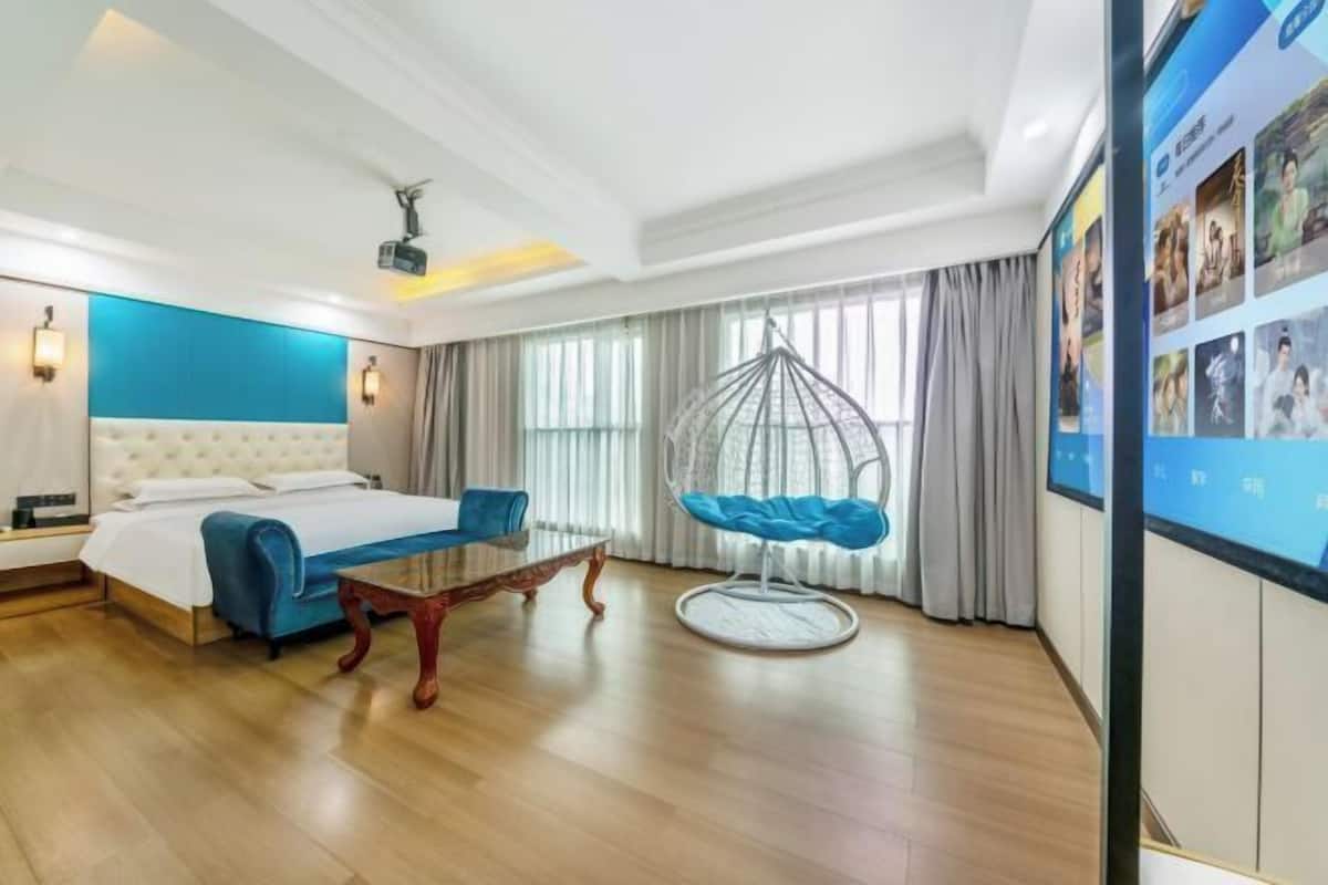 A hotel room with a bed, a dining table, a hanging chair, and a large screen displaying images.