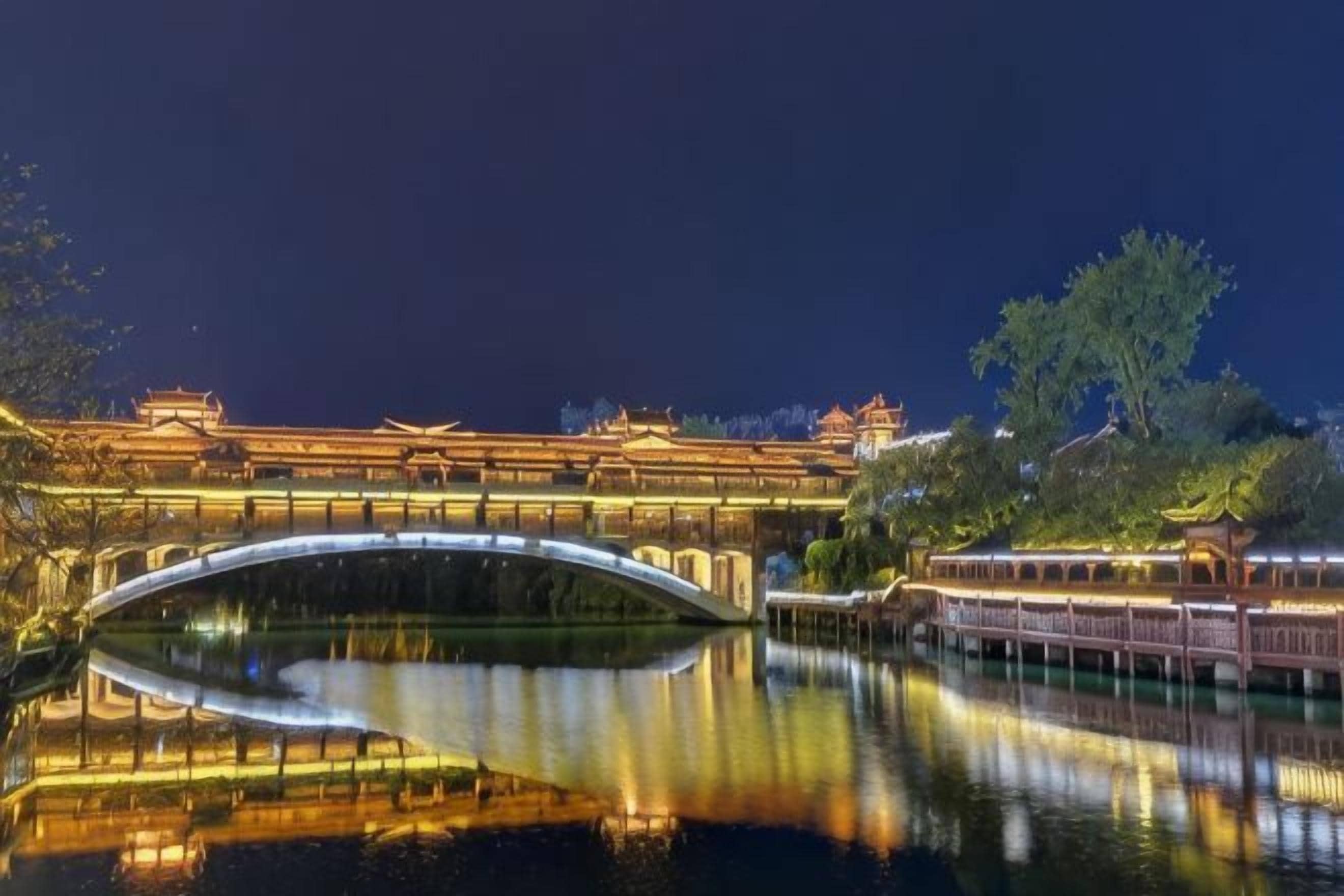Edificio tradicional con un puente sobre el agua, reflejando luces.
