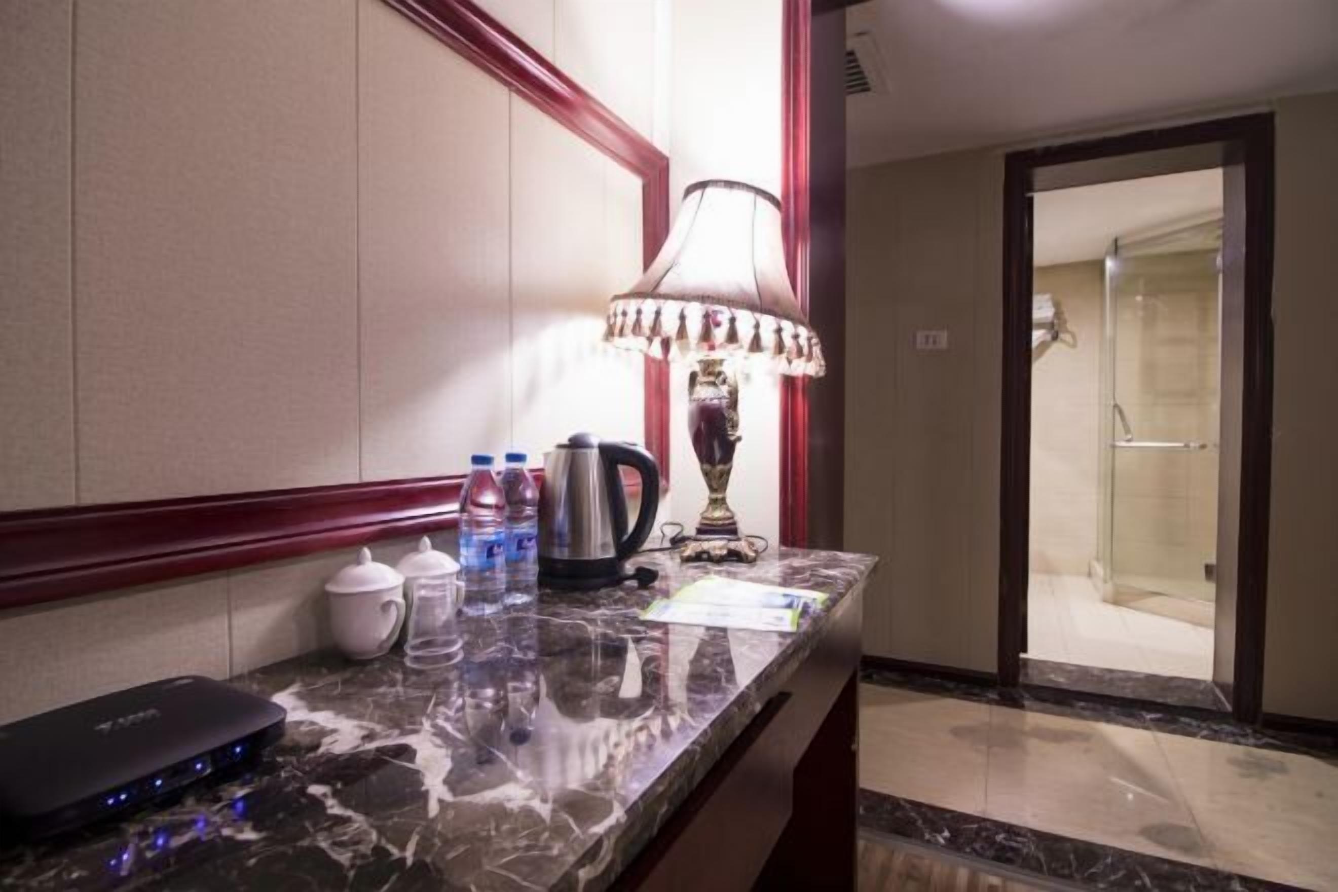 A hotel room with a marble countertop, a lamp, a kettle, a coffee maker, and a water dispenser.