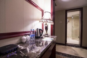 Habitación de hotel con encimera de mármol, lámpara, hervidor, cafetera y dispensador de agua.