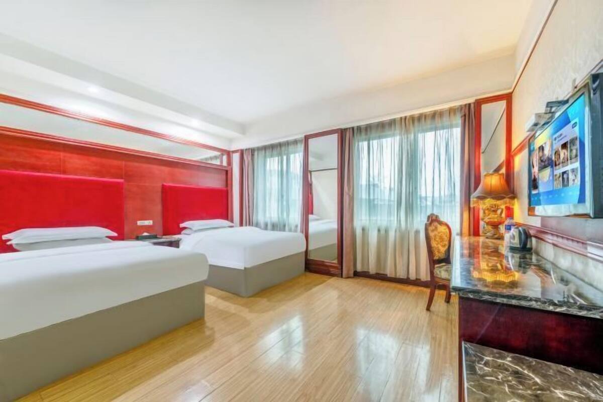 A hotel room with two beds, a desk, a chair, and a television.