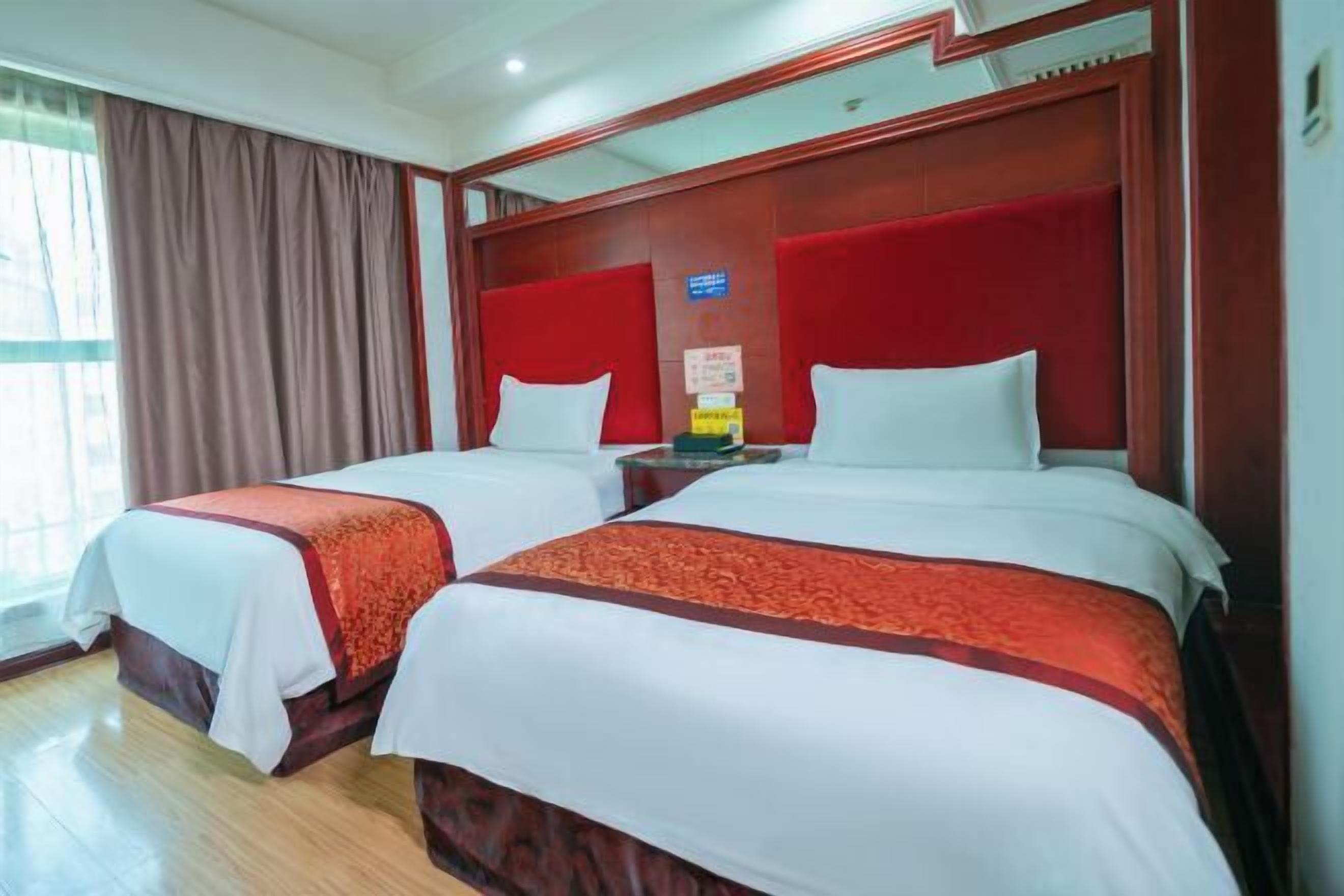 Une chambre d’hôtel avec deux lits, chacun doté de draps blancs et de touches de couleur rouge, d’une tête de lit en bois et d’une table de chevet avec une lampe.