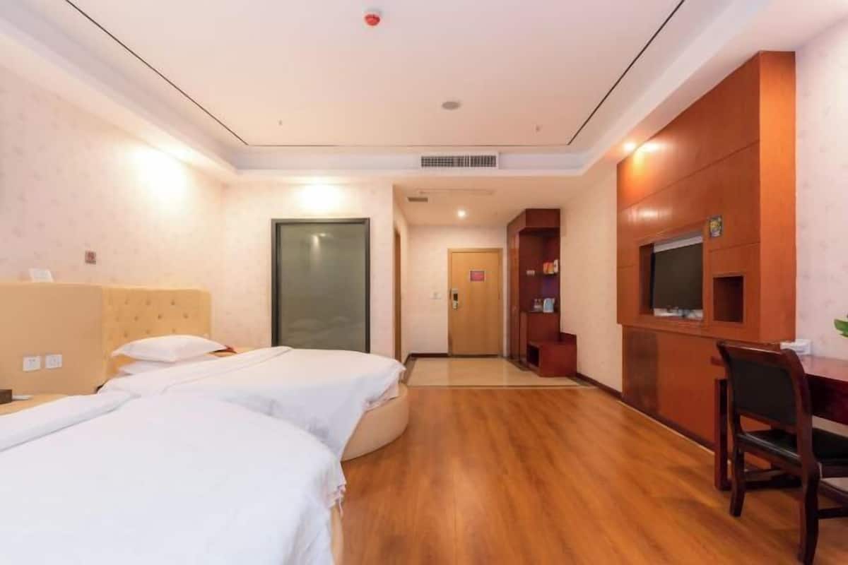 Une chambre d’hôtel avec deux lits, un bureau, une télévision et une porte donnant sur un couloir.