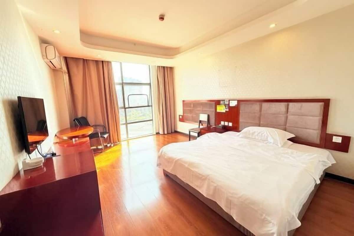 Une chambre d’hôtel avec un grand lit, un bureau, une chaise, une télévision et une fenêtre avec des rideaux.