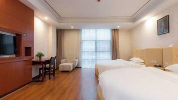 Una habitación de hotel con un escritorio de madera, dos camas, una silla y un ventanal grande.