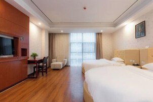 Una habitación de hotel con un escritorio de madera, dos camas, una silla y un ventanal grande.