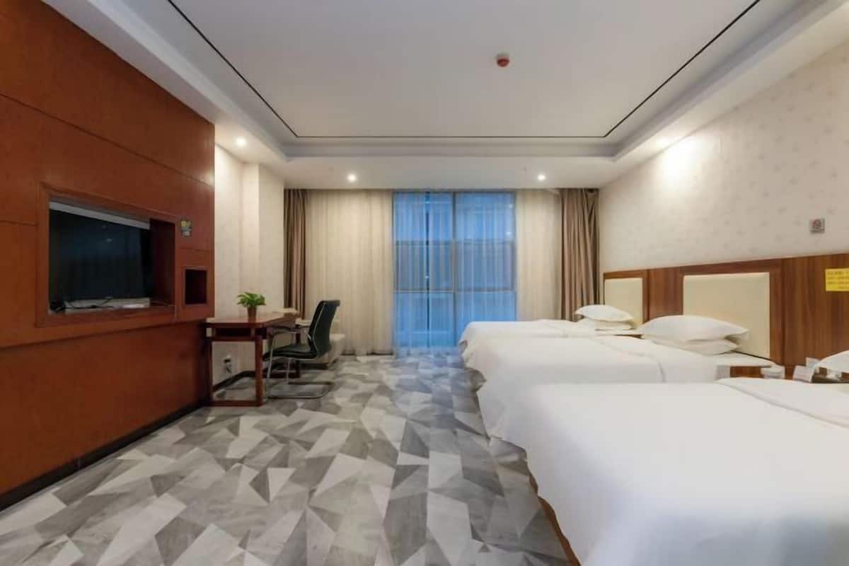 Une chambre d’hôtel équipée d’une télévision, d’un bureau avec une chaise, de deux lits et d’une grande fenêtre avec des rideaux.