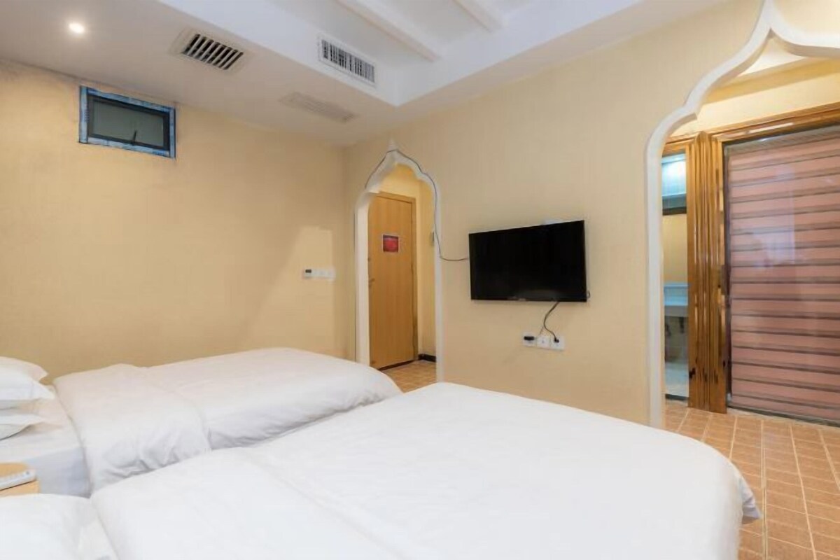 Habitación de hotel con dos camas, un televisor montado en la pared y una puerta que da a un pasillo.