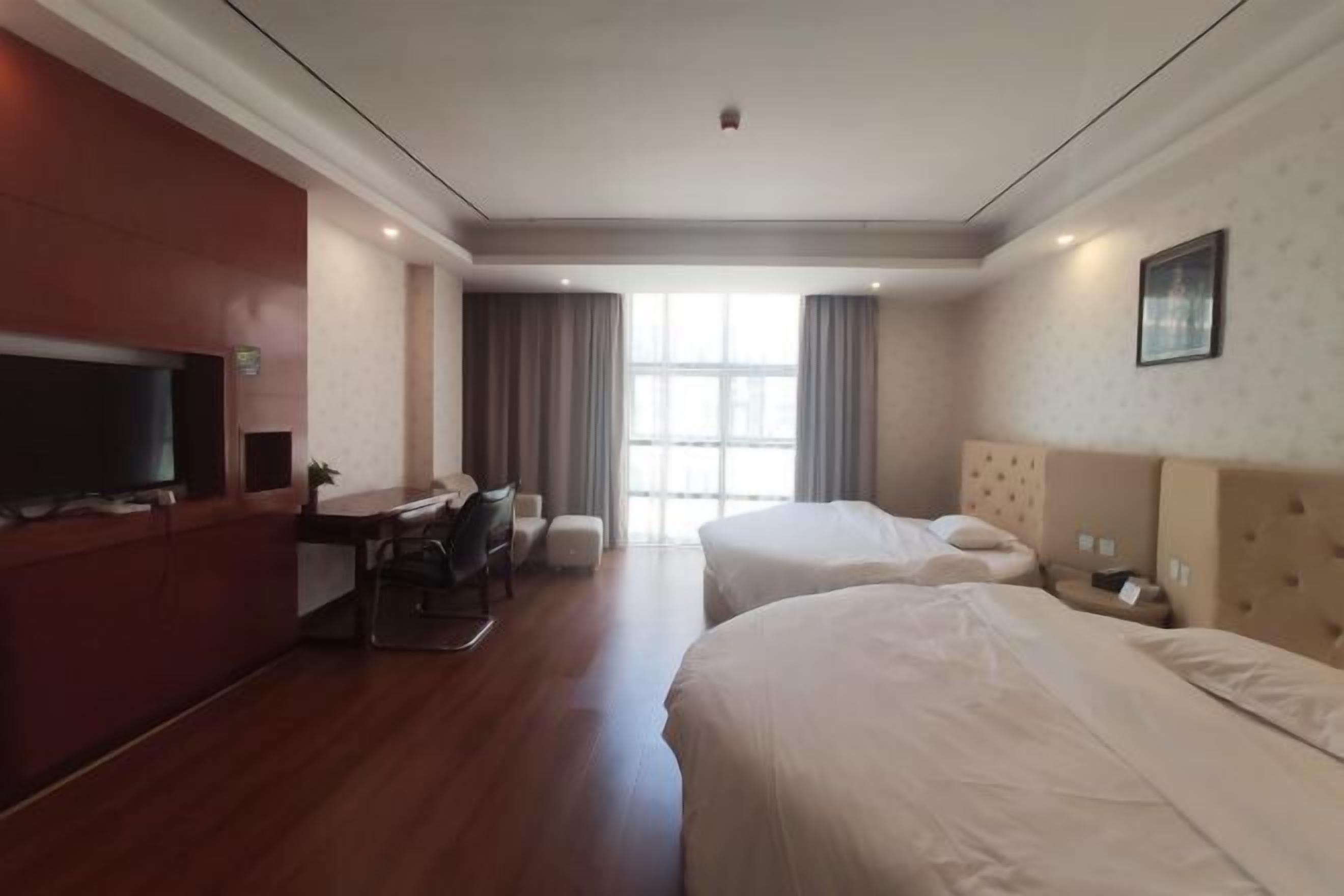 A hotel room with two beds, a desk, a chair, a TV, and a window with curtains.