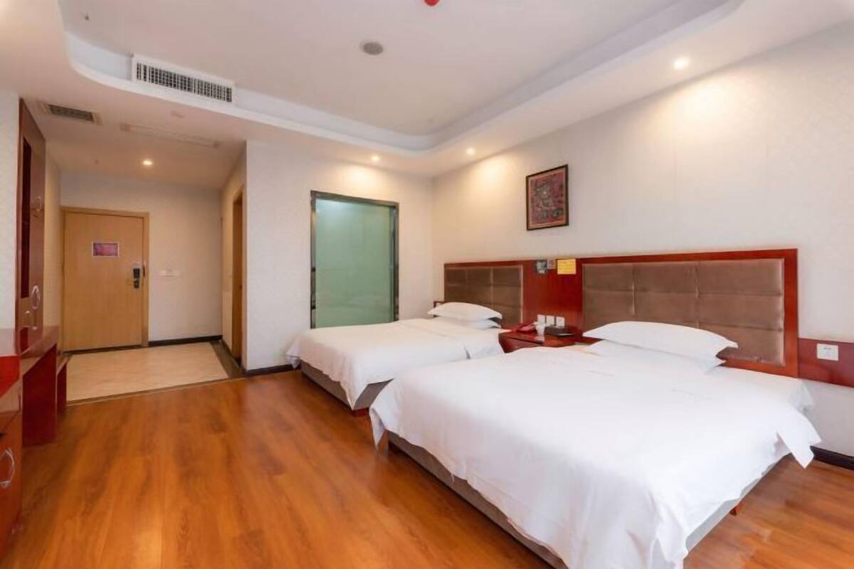 Une chambre d’hôtel avec deux lits, un plancher en bois, une porte et une œuvre d’art accrochée au mur.