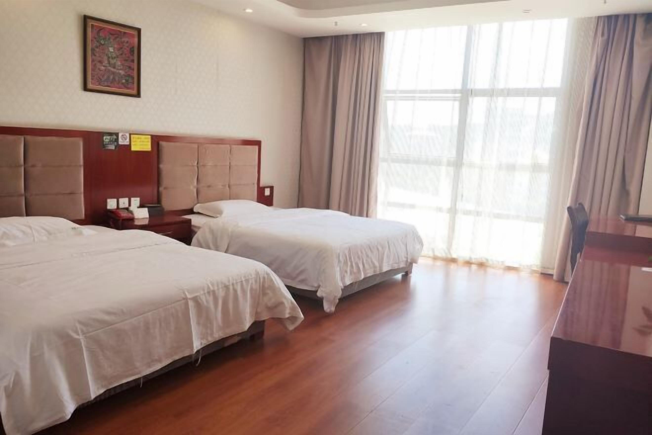 Ein Hotelzimmer mit zwei Betten, Holzboden, einem großen Fenster mit Vorhängen und einem Gemälde an der Wand.