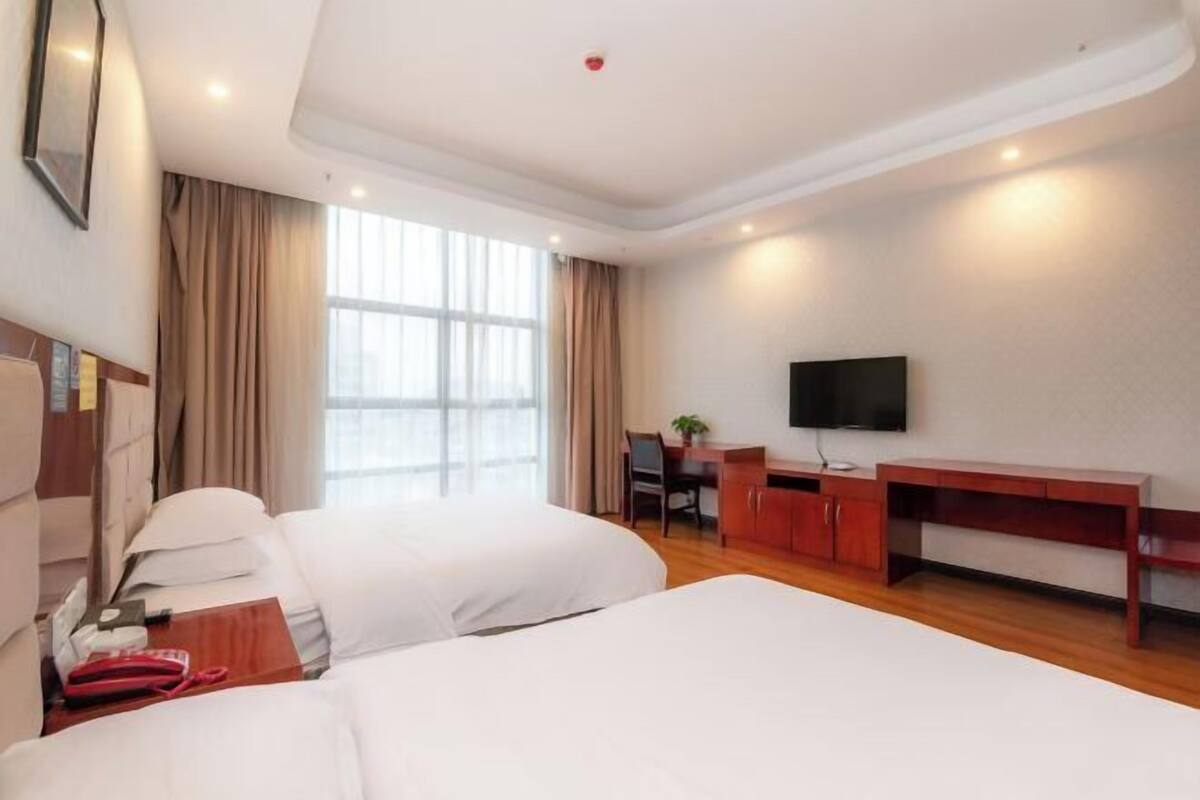 Une chambre d’hôtel avec deux lits, un bureau, une chaise, une télévision et une fenêtre avec des rideaux.