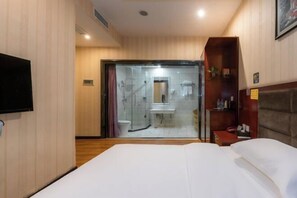 Una habitación de hotel con cama, televisión, baño con ducha y cabecero de madera.