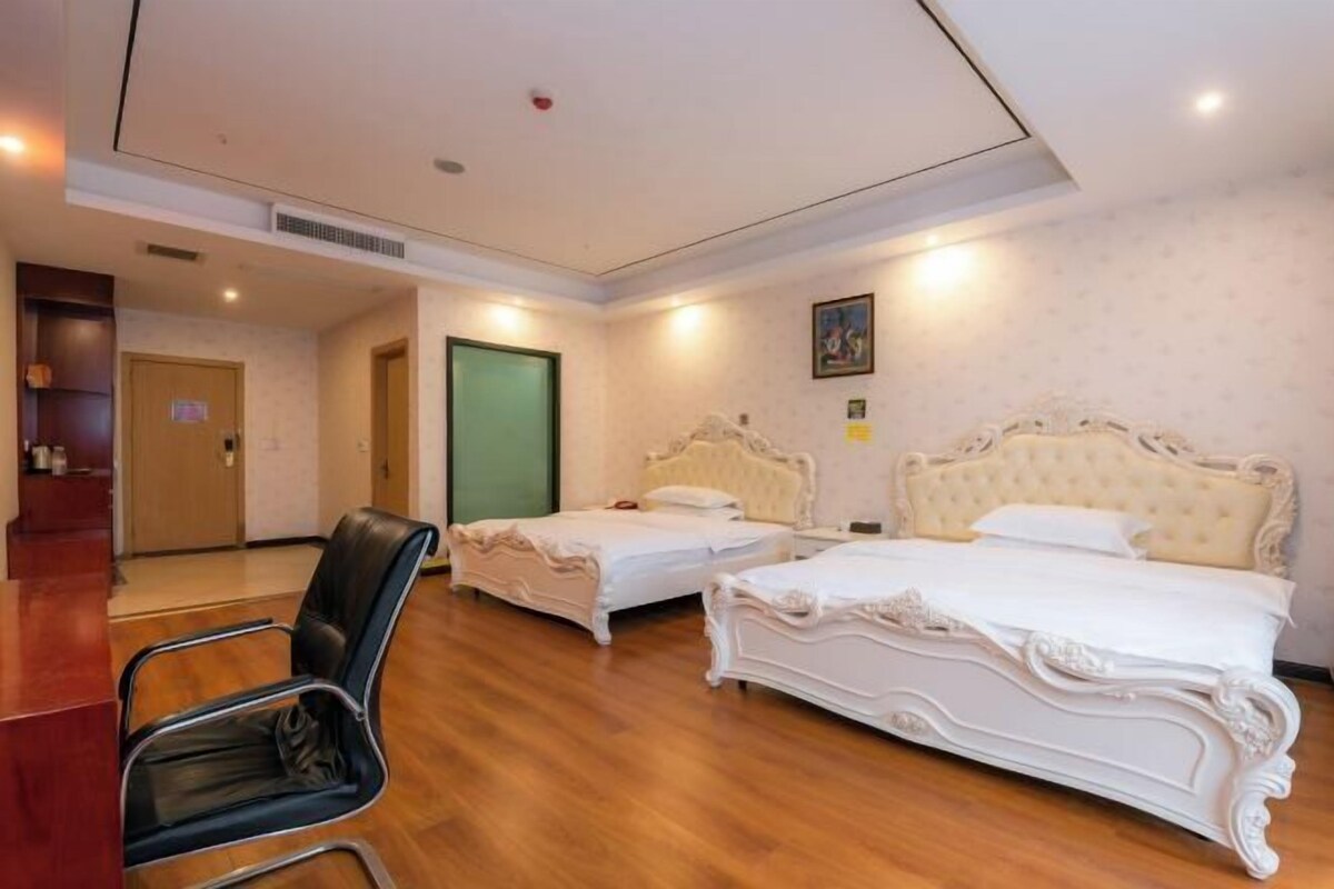 Habitación de hotel con dos camas, piso de madera, un escritorio con silla y una puerta verde.