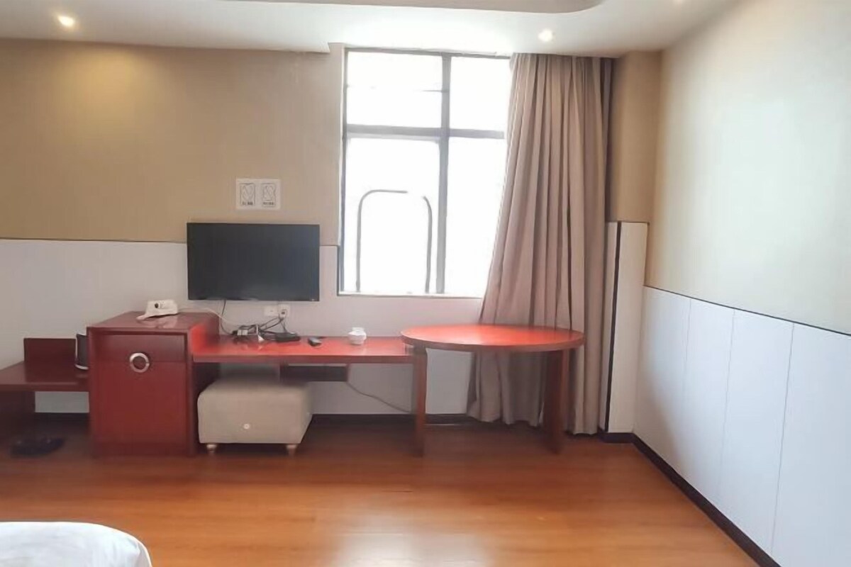 Una habitación de hotel con un escritorio de madera, televisor, ventana con cortinas y una cama.