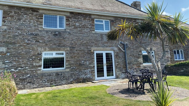Una casa de piedra con techo de tejas, una puerta principal y un patio con mobiliario exterior.