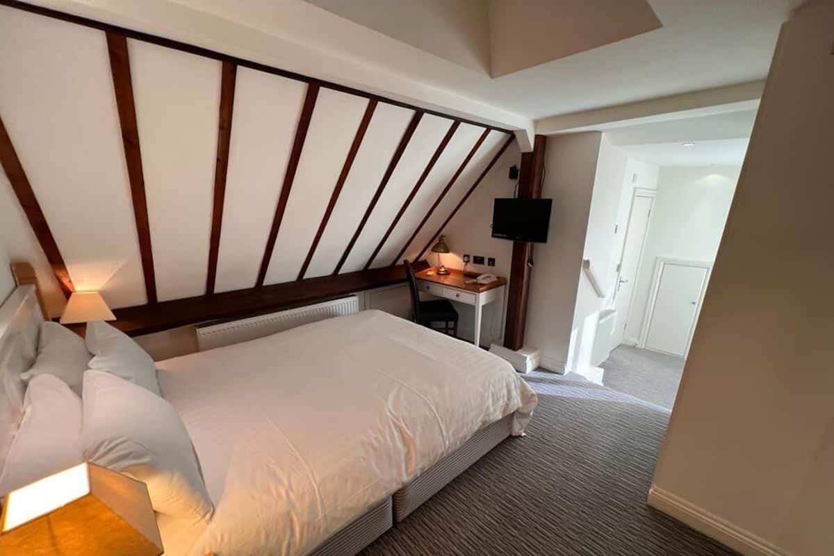 Una habitación de hotel con una cama grande, un escritorio con silla, un televisor de pantalla plana en la pared y una puerta que da a un pasillo.