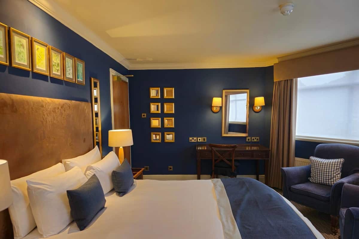 Una habitación de hotel con una cama grande, un escritorio, una silla y una ventana con cortinas.