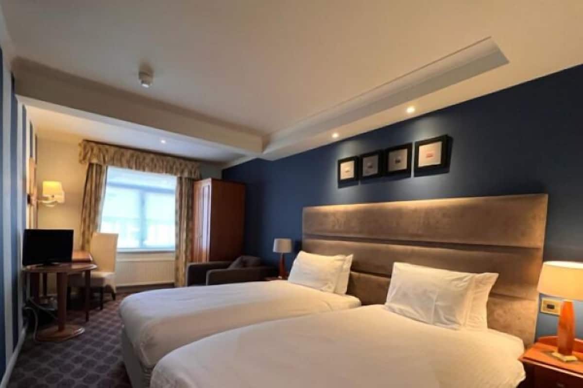 Habitación de hotel con dos camas, un escritorio, una silla, un televisor y una ventana con cortinas.