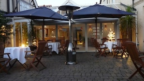 An outdoor dining area with tables and chairs, covered by umbrellas, and a central lamp post. - Hotel Manor - Datchet (Slough)