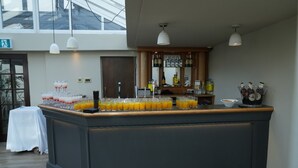 A bar area with a long counter, glasses of orange juice, and bottles of alcohol. - Hotel Manor - Datchet (Slough)