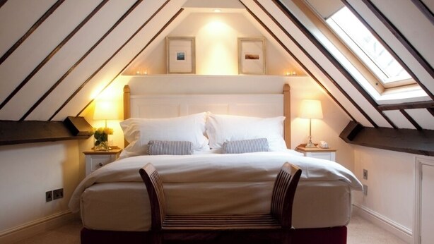 A bedroom with a sloped ceiling, a bed with white bedding, two bedside lamps, and framed pictures above the bed. - Hotel Manor - Datchet (Slough)