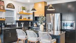 Una cocina moderna con armarios oscuros, electrodomésticos de acero inoxidable y una isla central con taburetes de bar.
