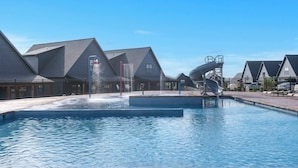 Una piscina con una fuente de agua, rodeada de edificios modernos con techos inclinados.