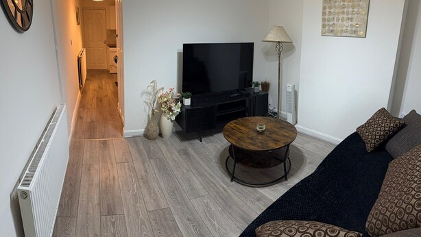 A living room with a TV, sofa, coffee table, and a hallway leading to a kitchen. - F2S Serviced 2Bed House Wi-fi, Netflix, Parking, Train station nearby. Holiday! (Derby)