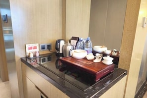 Une chambre d’hôtel avec un meuble en bois, une table avec un plateau en verre et un service à thé, une bouilloire et des bouteilles d’eau.