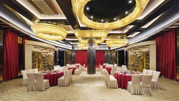 A banquet hall with round tables, red curtains, and a chandelier.
