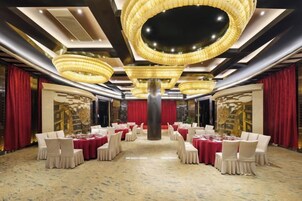 Un salón de banquetes con mesas redondas, cortinas rojas y un candelabro.