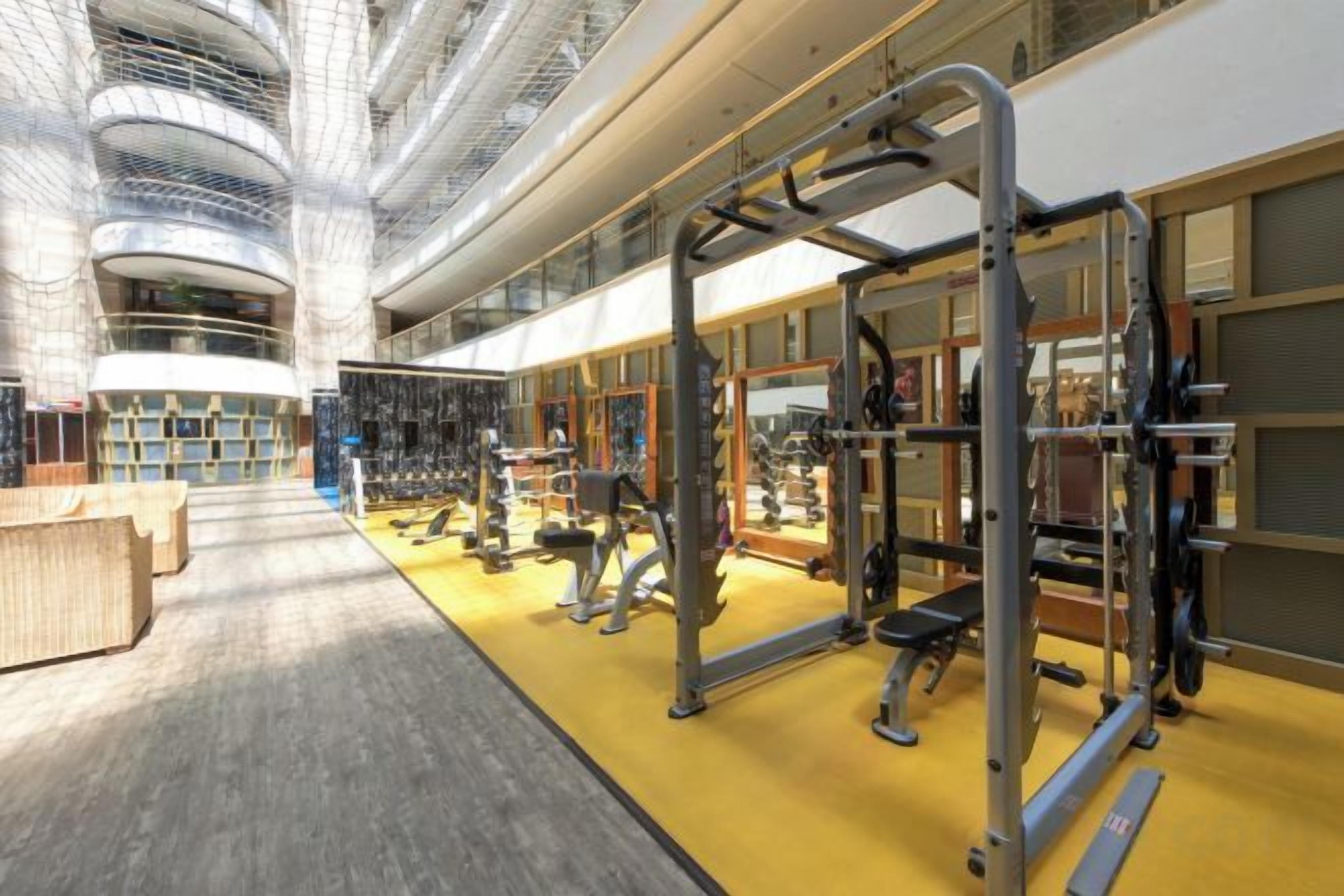 A gym with various exercise equipment, a yellow floor, and a high ceiling with a unique architectural design.