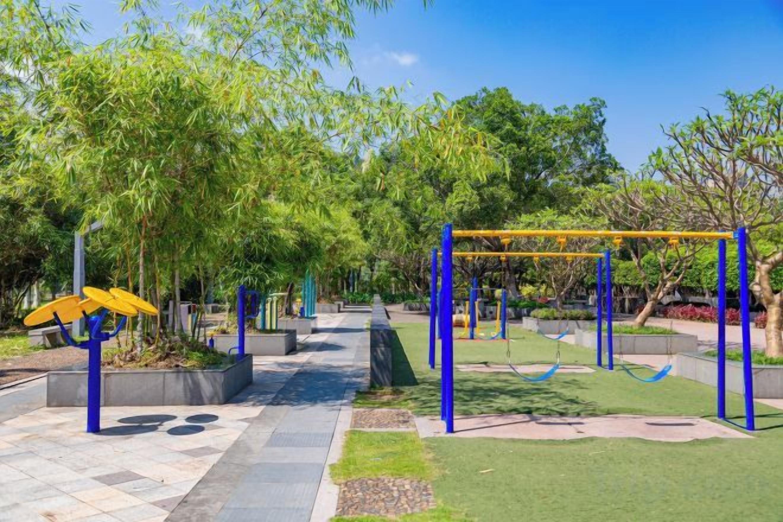 Un parque infantil con columpios y una estructura para escalar, rodeado de árboles y un camino pavimentado.