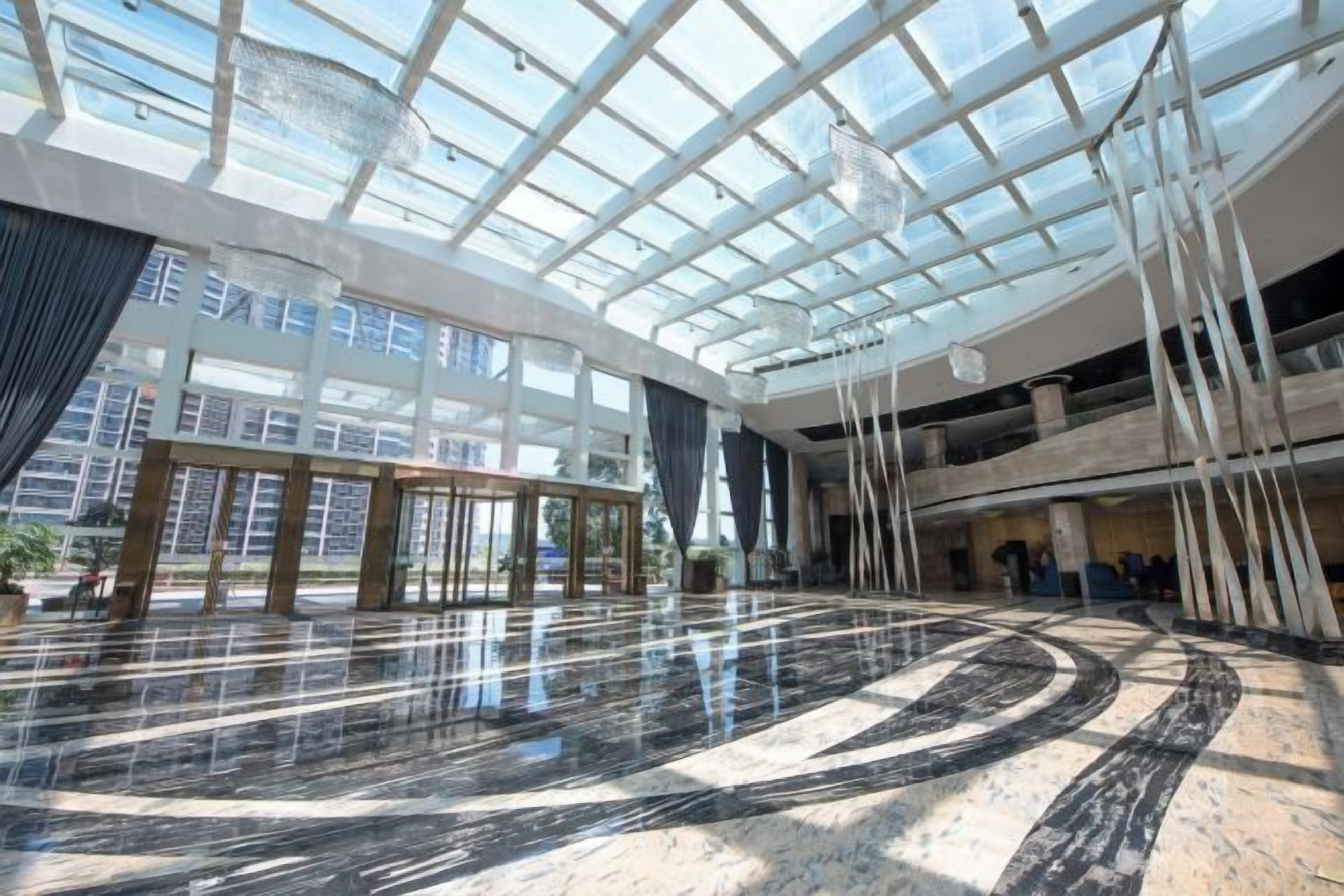 A spacious atrium with a high ceiling and a glass roof, featuring a polished marble floor and modern furnishings.