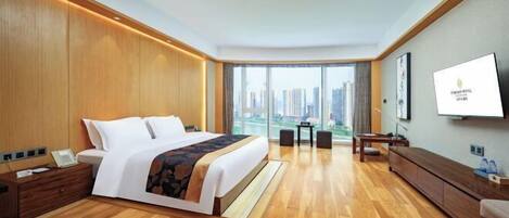 A hotel room with a large bed, a desk, a chair, a TV, and a view of the city.