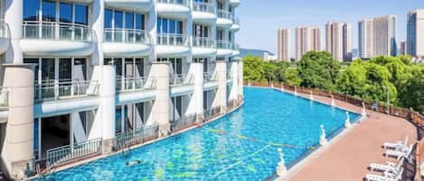 Una piscina adiacente a un edificio moderno con balconi, immersa in un’area verde con lettini.