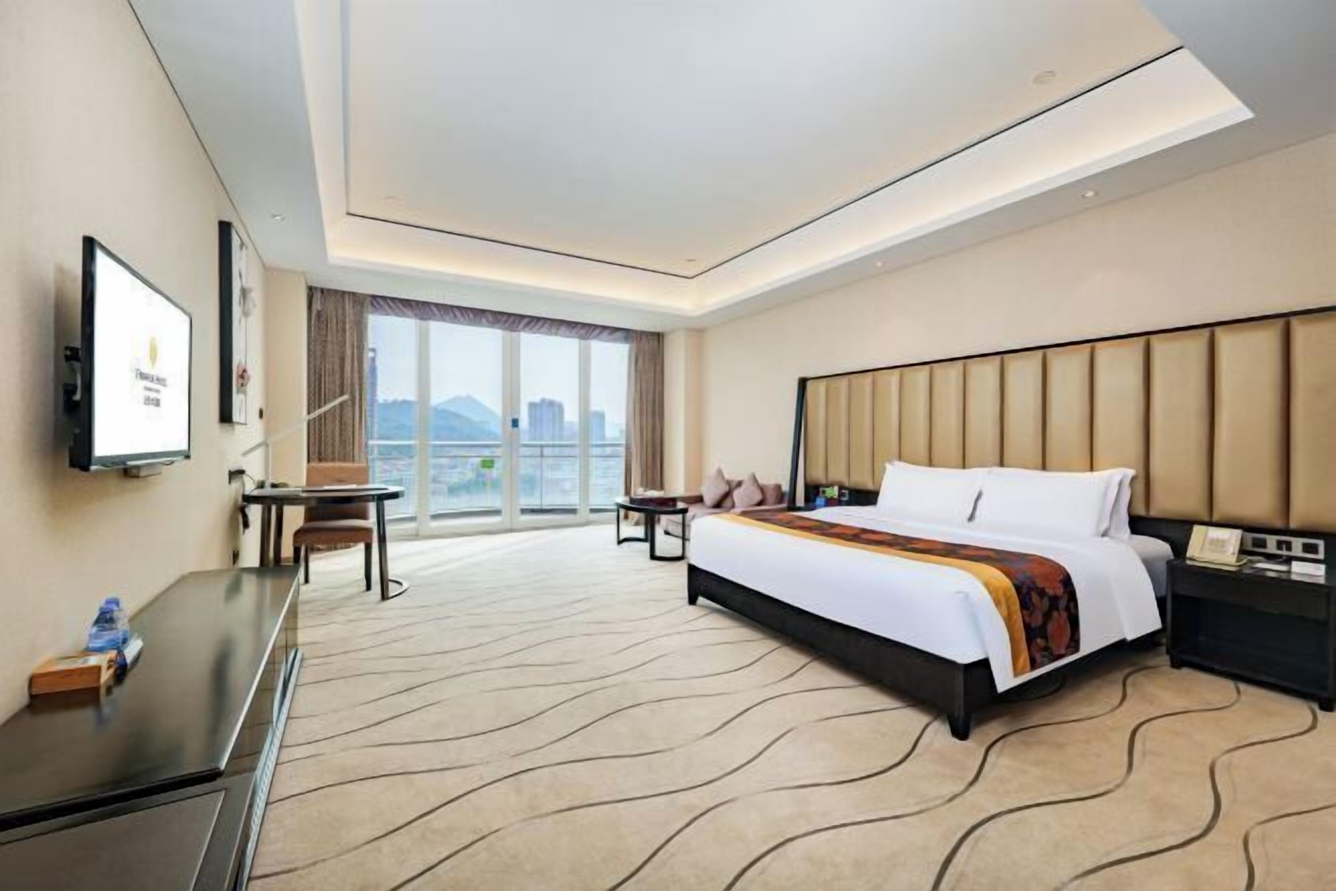 A hotel room with a large bed, a desk, a chair, a TV, and a city view.