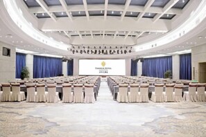 Un salón de conferencias con filas de sillas, un escenario con una pantalla y un amplio suelo alfombrado.