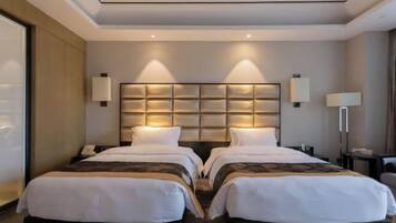 A hotel room with two beds, a large padded headboard, bedside lamps, and a desk with a chair.