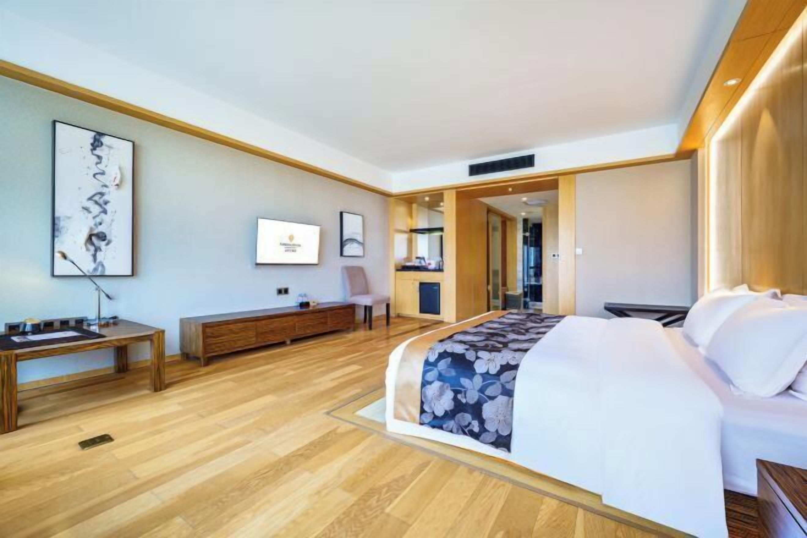 A modern hotel room with a large bed, wooden flooring, a desk, and a television.