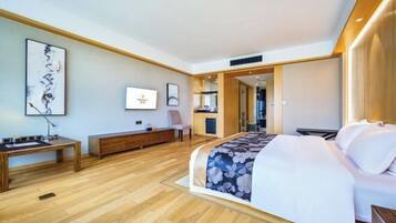 A modern hotel room with a large bed, wooden flooring, a desk, and a television.