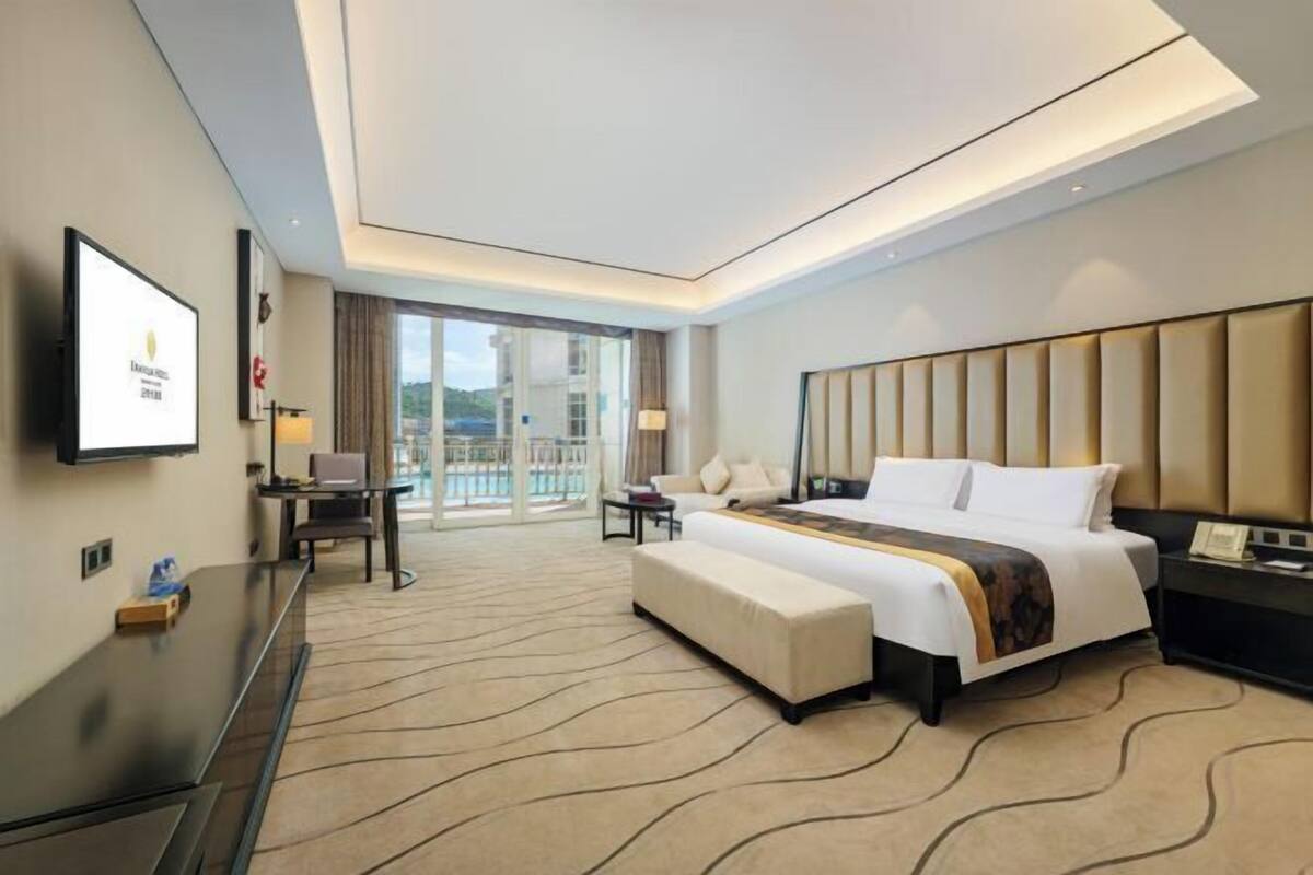 A modern hotel room with a large bed, a desk, a chair, and a TV mounted on the wall.