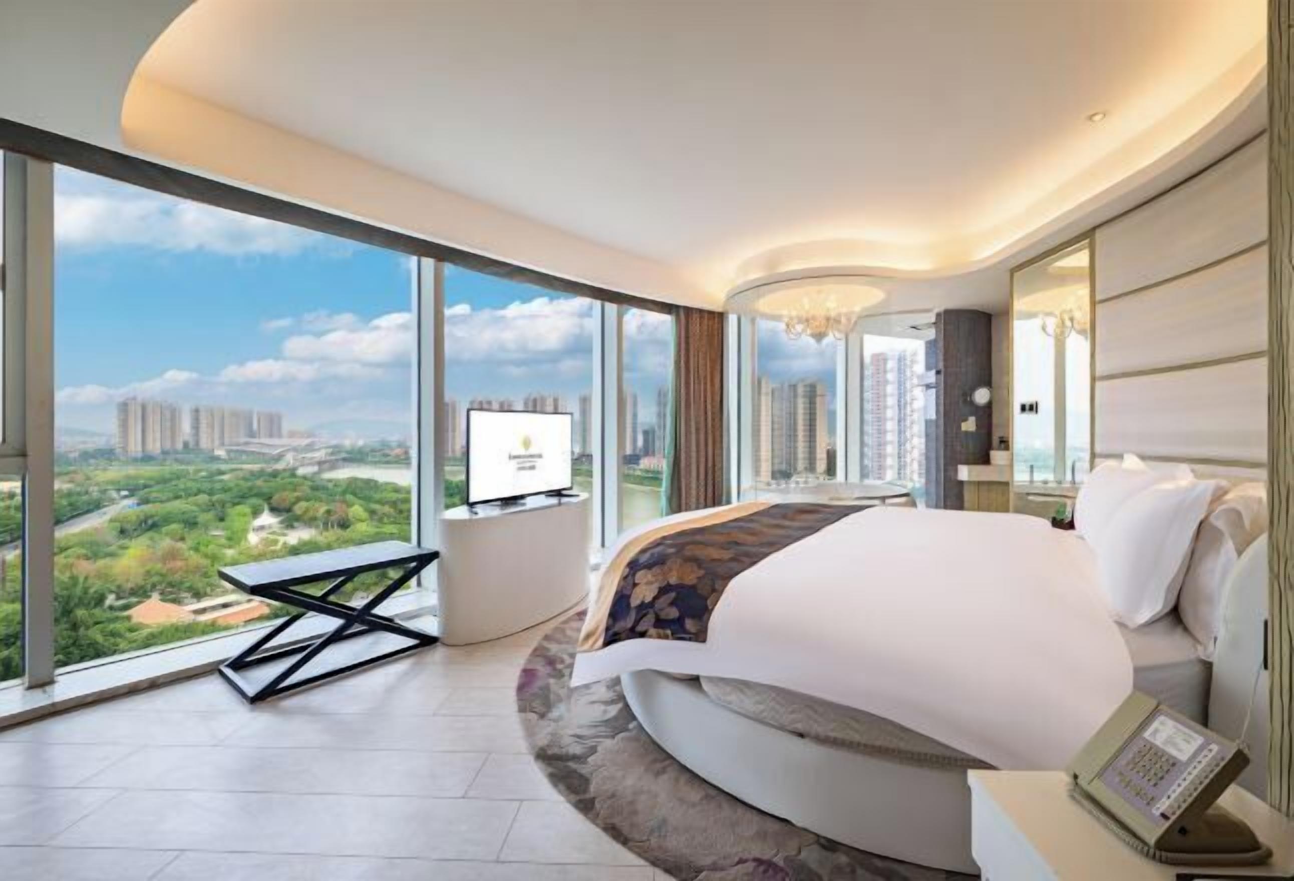 A modern hotel room with a large bed, a TV, and a city view.