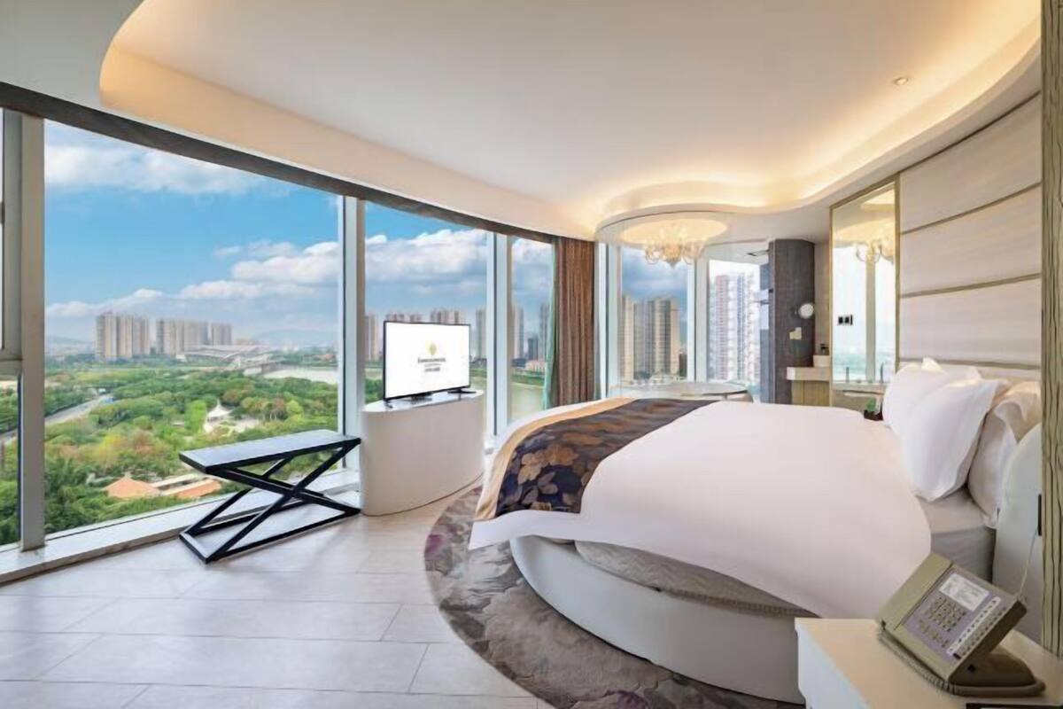 A modern hotel room with a large bed, a TV, and a city view.