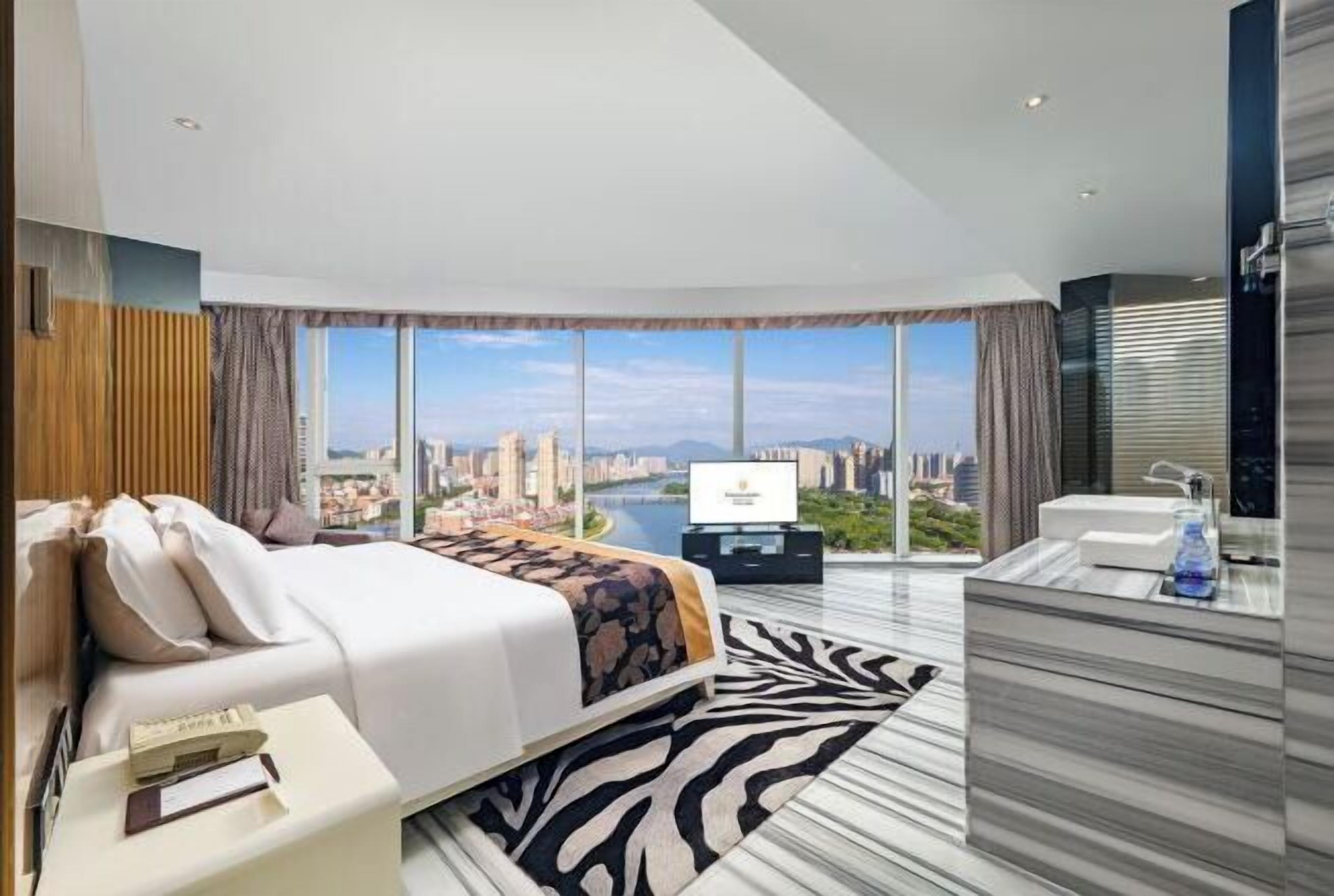 A modern hotel room with a large bed, a TV, a bathroom with a marble countertop, and a city view.