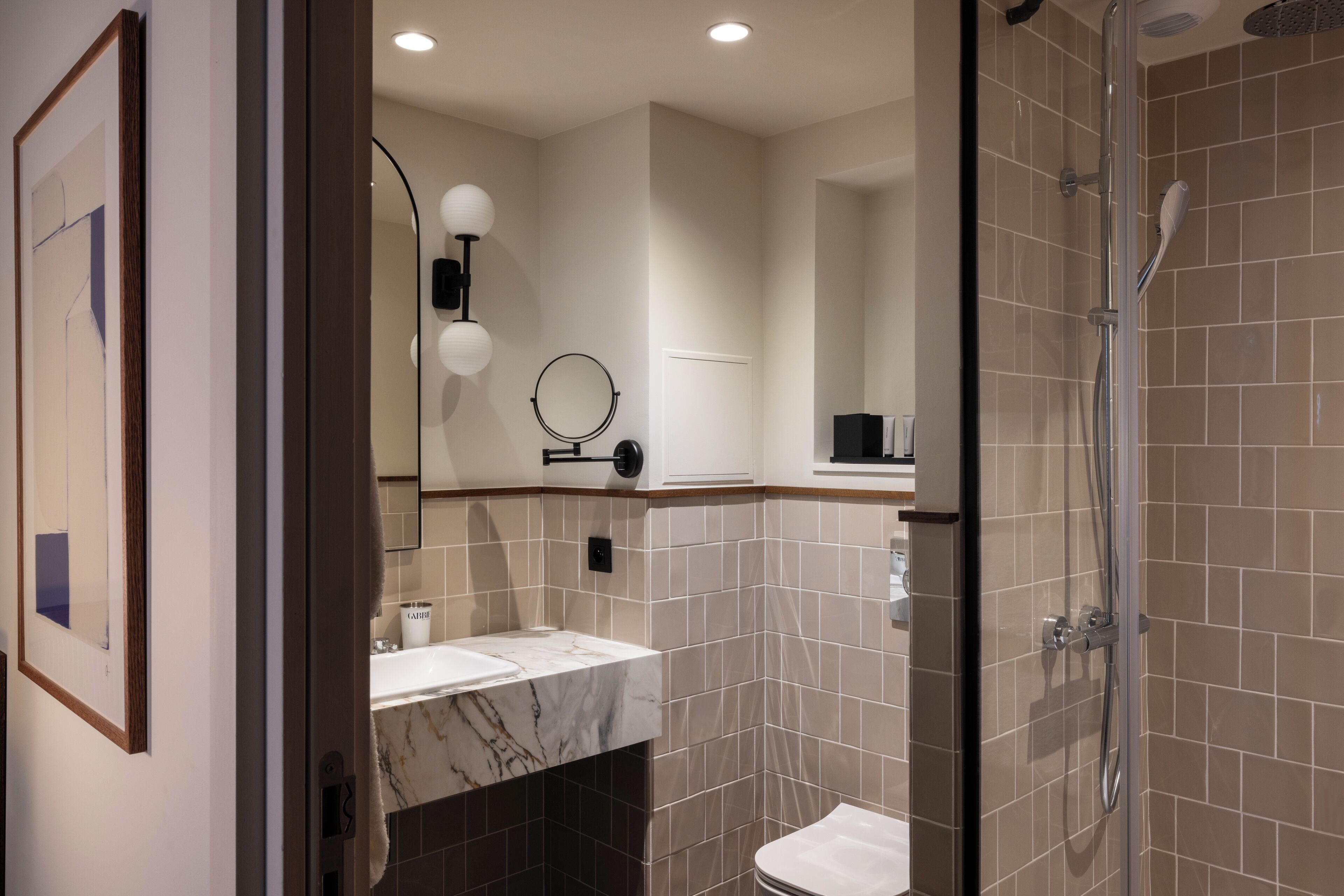 Une salle de bain moderne avec une douche à parois de verre, un lavabo en marbre et un miroir doté d’un cadre rond.