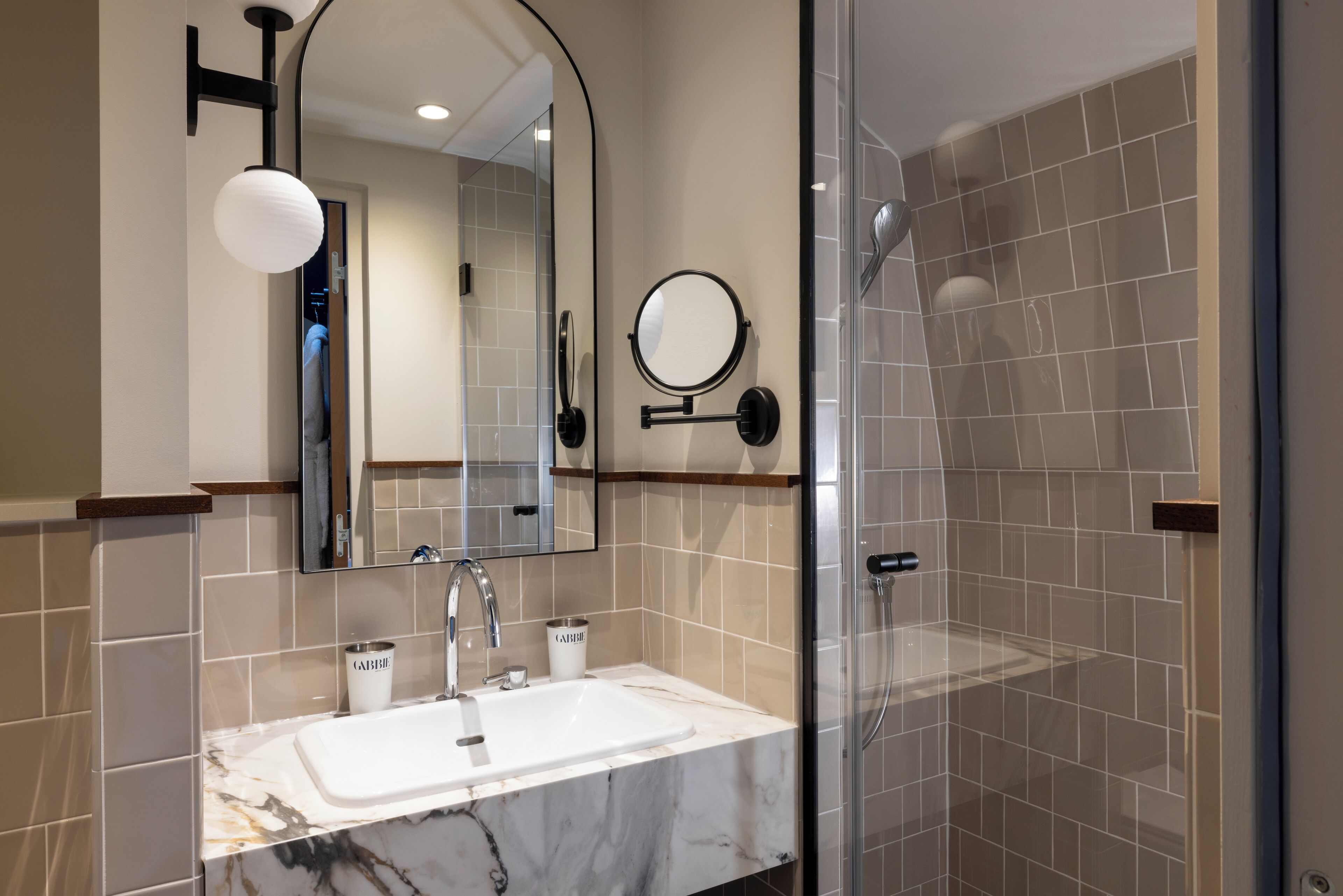 Un baño moderno con un lavamanos blanco, un espejo redondo y un cabezal de ducha de mano.
